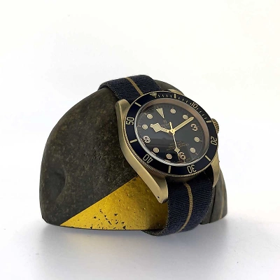 TUDOR Black Bay Heritage - Uhr am Textilband, befestigt an einem Stein mit goldenem Element, das die Farbe des Bronze-Gehäuses aufnimmt